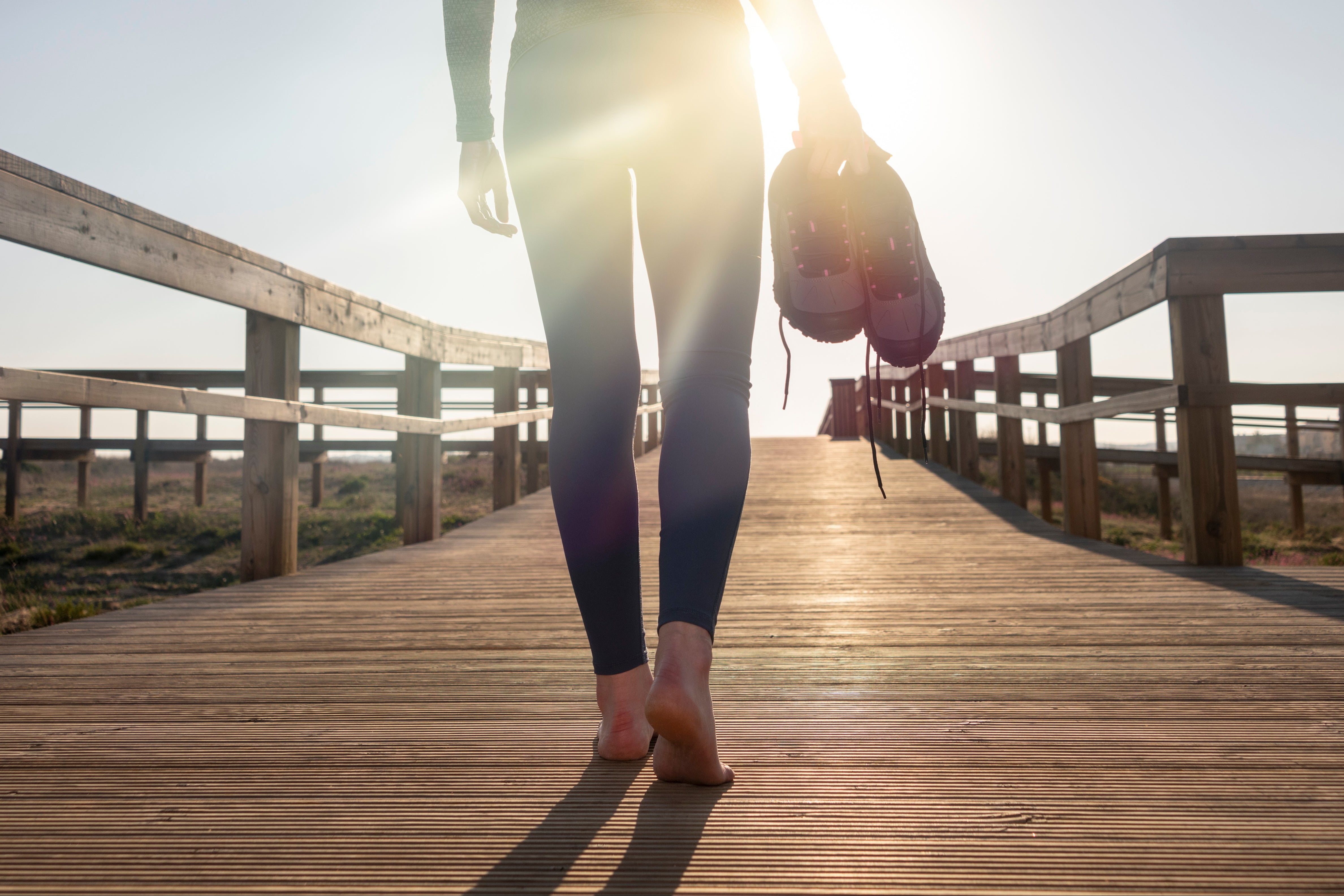 Runner walking outdoors on a boardwalk with sunlit shoes and heels, representing athletic foot health, dry heel recovery, and natural skincare routine.