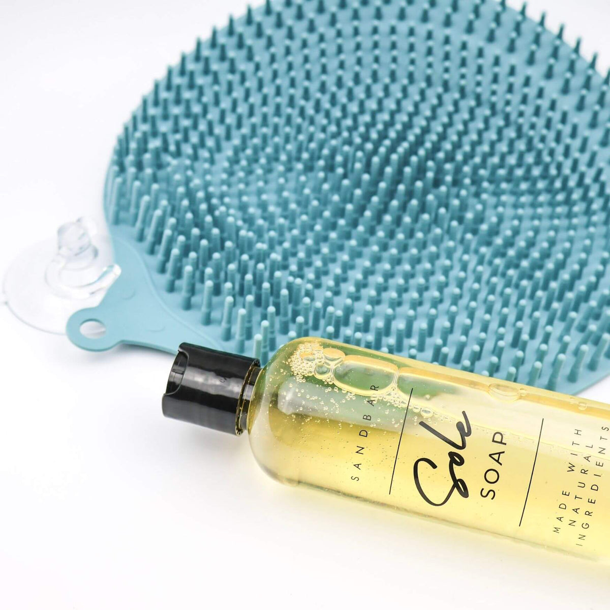 Close-up of SandBar Foot Scrubber Mat in Morning Glory teal with a bottle of Sole Soap resting on it
