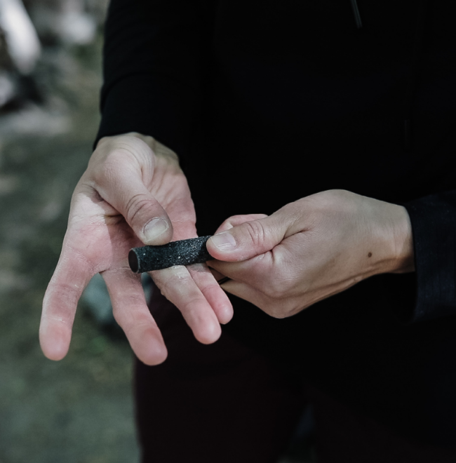 Hands holding the 4" Quickie black callus file. Which is a smaller version of the original Sandbar filing down calluses on their fingers instead of using  a callus shaver or callus remover.