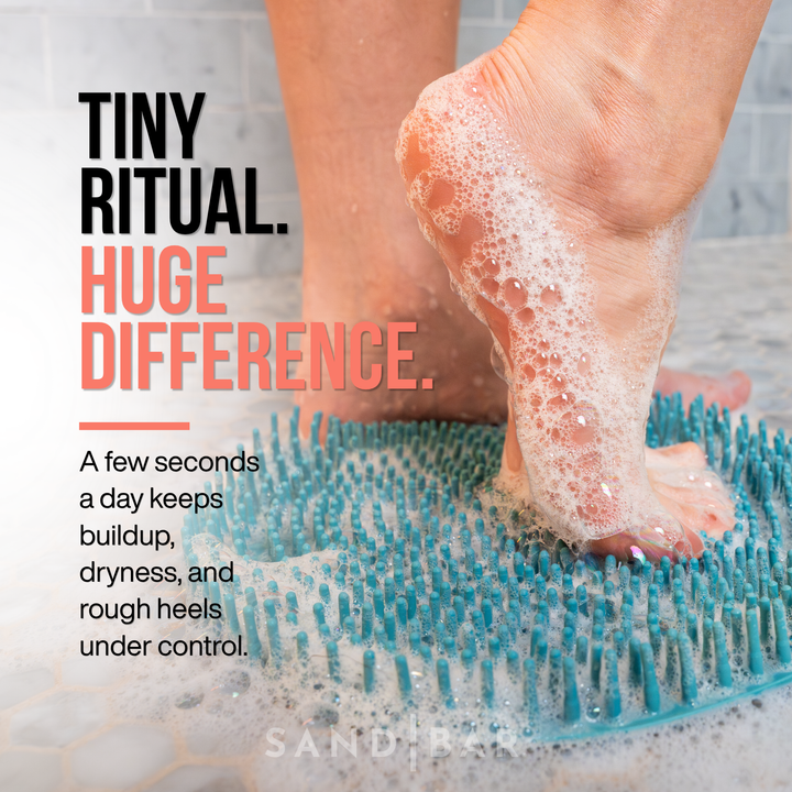Woman using SandBar foot scrubber mat with soap lather in shower for daily exfoliation and soft heel maintenance.