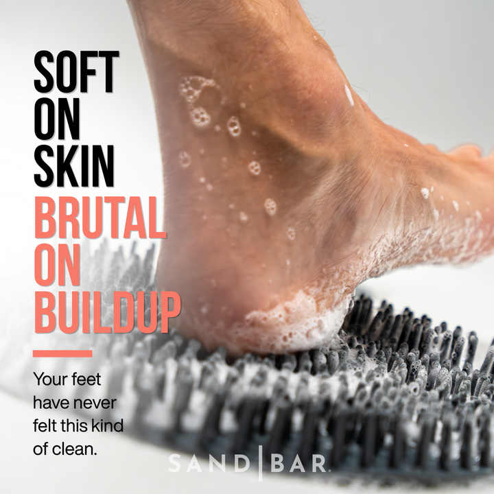 Close-up of heel exfoliation using a shower foot scrubber to remove buildup and soften rough dry calloused feet.