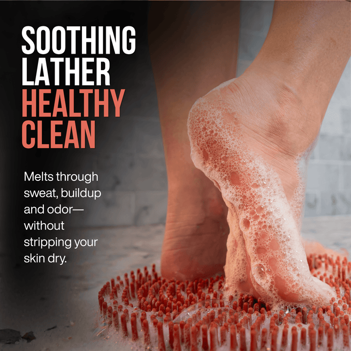 A close-up of a woman's foot stepping onto a foot scrubber with Rich, satisfying lather from SandBar Sole Soap cleans away sweat, buildup, and odor while leaving feet soft, healthy, and refreshed. with promotional text reading 'SOOTHING LATHER HEALTHY CLEAN'.